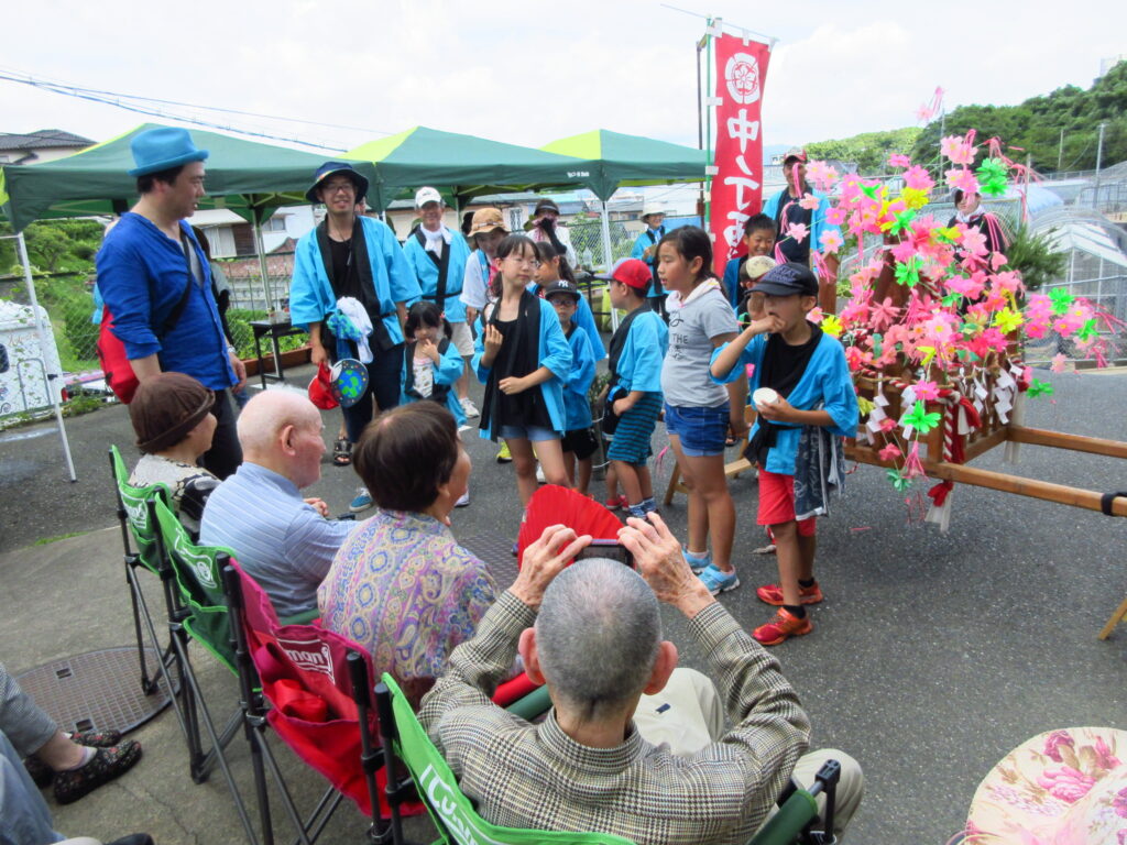 施設利用者と職員が夏祭りのような屋外イベントに参加している風景
